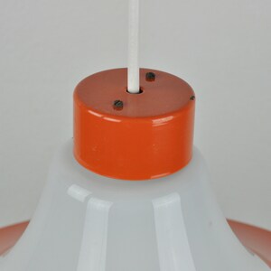 May include: Close-up of a white and orange pendant light fixture. The fixture has a white, bell-shaped shade and an orange, cylindrical top.