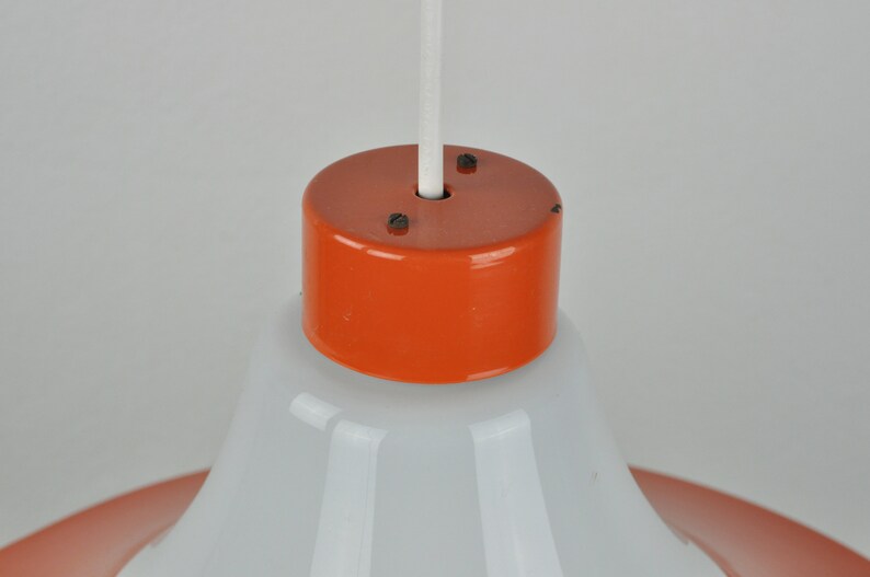 May include: Close-up of a white and orange pendant light fixture. The fixture has a white, bell-shaped shade and an orange, cylindrical top.