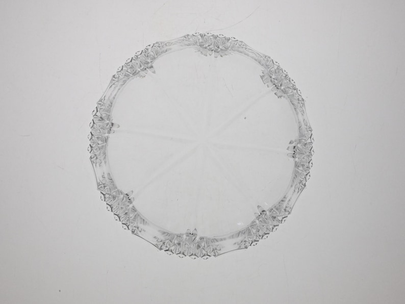 May include: A clear glass cake plate with a decorative, scalloped edge.