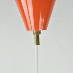 May include: Close-up of an orange ceramic lampshade with a white cord hanging from the bottom.