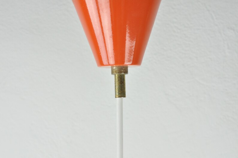 May include: Close-up of an orange ceramic lampshade with a white cord hanging from the bottom.