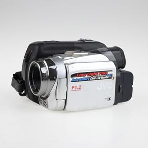 Puede incluir: Una videocámara MiniDV JVC de color plata y negro con un objetivo asférico F1.2. El panel lateral muestra el texto Low Light Plus, Data Battery, Clear LCD Monitor y MiniDV. El dispositivo incluye una correa de mano negra y una carcasa.