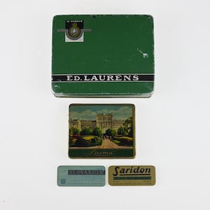 May include: A collection of four vintage metal tins including a large green rectangular Ed. Laurens tin, a medium rectangular tin featuring a building illustration, and two small rectangular tins labelled Slovalgin and Saridon respectively.