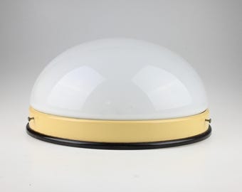 May include: A dome-shaped ceiling light fixture featuring a smooth white glass shade. The base is composed of a pale yellow metal band secured with small side screws, resting on a thin, circular black metal rim at the bottom edge.
