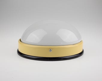 May include: A dome-shaped ceiling light fixture featuring a smooth white glass shade, a pale yellow circular metal band, and a black base. The fixture is secured with a small silver-colored metal screw visible on the side of the yellow band.