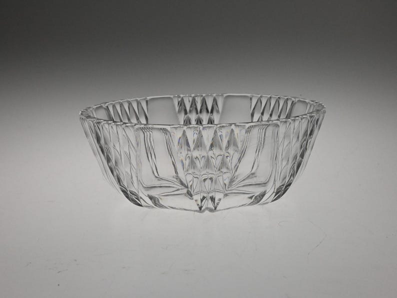 May include: A clear glass bowl with a diamond-shaped pattern. The bowl is empty and has a smooth, polished surface.