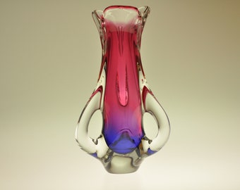 Può includere: Un vaso di vetro rosa e blu con un design astratto unico. Il vaso ha una base in vetro trasparente e due manici.