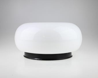 May include: A mushroom-shaped table lamp featuring a smooth, opaque white glass dome shade resting on a circular, solid black metal base. The lamp has a rounded, low-profile silhouette with a glossy finish on the glass and a matte black finish.