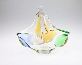 May include: A clear glass bowl with an irregular, organic shape featuring translucent accents of yellow, blue, and green. The bowl has a thick, solid base and a wide, undulating rim that rises to a central point, creating a sculptural appearance.