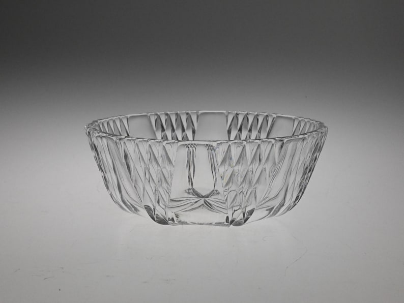 May include: A clear glass bowl with a decorative, diamond-shaped pattern. The bowl is round and has a wide, shallow shape.