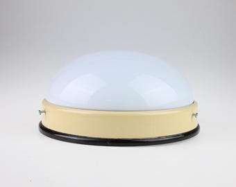 May include: A dome-shaped ceiling light fixture featuring a smooth white glass shade, a cream-colored metal base, and a thin black circular trim at the bottom. Two small silver-toned metal screws are visible on the sides of the base.