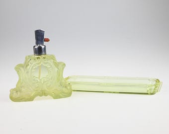 May include: A pale yellow glass perfume bottle with an ornate, raised scrollwork pattern and a silver-toned metal atomizer pump, accompanied by a matching rectangular pale yellow glass tray with a decorative border and smooth finish.