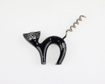 May include: A black cat-shaped corkscrew with a glossy finish and white speckled details. The cat is depicted in an arched pose with a silver-colored metal spiral tail extending upwards, designed for removing corks from wine bottles.