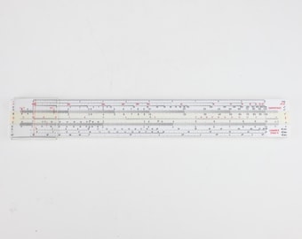 May include: A white slide rule with a clear plastic cursor featuring a red hairline. The device displays multiple numerical scales in black and red ink, with the text Logarex 27203-A printed on the right side of the body.