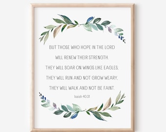 May include: A framed print with a light wood frame. The print features text from Isaiah 40:31, surrounded by a watercolor wreath of green and blue leaves. The text reads, "But those who hope in the Lord will renew their strength."