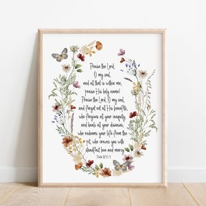 May include: A framed print featuring a floral wreath design with butterflies and text. The text reads "Praise the Lord, O my soul..." in a script font. The frame is a light wood color, and the artwork has a watercolor style.