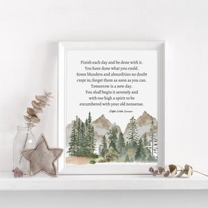 Op de afbeelding: Een ingelijst afdruk met een aquarel-illustratie van een bergketen met dennenbomen en mist. De afdruk bevat een citaat van Ralph Waldo Emerson: &bdquo;Maak elke dag af en wees er klaar mee. Je hebt gedaan wat je kon. Er zijn ongetwijfeld wat fouten en absurditeiten ingeslopen; vergeet ze zo snel mogelijk. Morgen is een nieuwe dag. Je zult hem rustig beginnen en met een te hoge geest om belast te worden met je oude onzin.&ldquo;