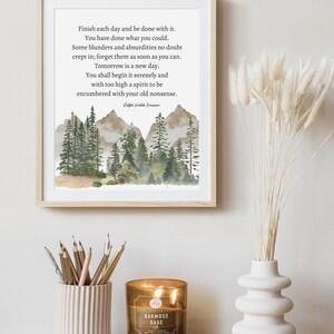 Op de afbeelding: Een ingelijst drukwerk met een aquarel-illustratie van een boslandschap en een citaat van Ralph Waldo Emerson: &bdquo;Maak elke dag af en wees er tevreden mee. Je hebt gedaan wat je kon. Er zijn ongetwijfeld wat fouten en absurditeiten ingeslopen; vergeet ze zo snel mogelijk. Morgen is een nieuwe dag. Je zult hem rustig beginnen en met een te hoge geest om belast te worden met je oude onzin. &ldquo;