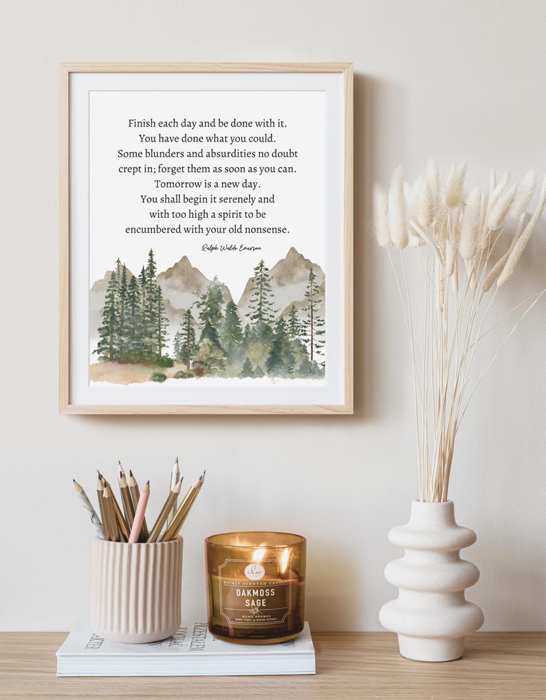 Op de afbeelding: Een ingelijst drukwerk met een aquarel-illustratie van een boslandschap en een citaat van Ralph Waldo Emerson: &bdquo;Maak elke dag af en wees er tevreden mee. Je hebt gedaan wat je kon. Er zijn ongetwijfeld wat fouten en absurditeiten ingeslopen; vergeet ze zo snel mogelijk. Morgen is een nieuwe dag. Je zult hem rustig beginnen en met een te hoge geest om belast te worden met je oude onzin. &ldquo;