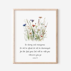 May include: A framed print with a watercolour illustration of wildflowers in blue, red, white, and yellow. The text "Be strong and courageous" and a Bible verse are printed below the floral image.