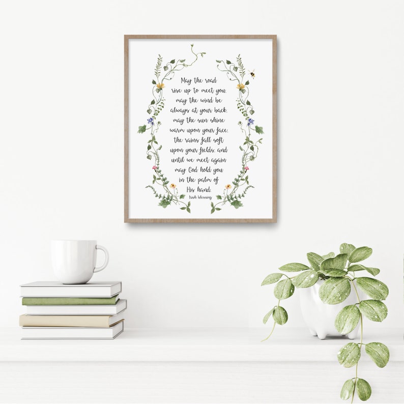May include: A framed print with a white background and a floral border. The print features a poem about hope and faith with the text "May the road rise up to meet you, may the wind be always at your back, may the sun shine warm upon your face. The rains fall soft upon your fields, and until we meet again may God hold you in the palm of His hand.  Josh Blooming."