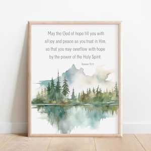 May include: A framed print with a watercolor painting of a forest reflecting in a lake. The print features the Bible verse "May the God of hope fill you with all joy and peace as you trust in Him, so that you may overflow with hope by the power of the Holy Spirit." Romans 15:13