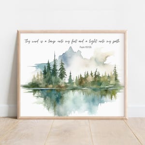 May include: A framed watercolour print depicting a tranquil landscape with a mountain, trees, and a lake. The artwork uses shades of green, blue, and grey. The text "Thy word is a lamp unto my feet and a light unto my path. Psalm 119:105" is written at the top.
