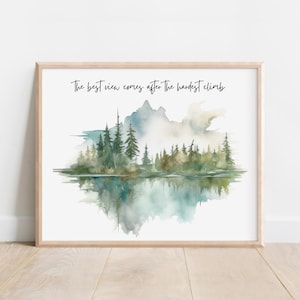 May include: A framed watercolor print featuring a serene landscape with a mountain range, trees, and a reflective lake. The artwork is in shades of green, blue, and white, with the text "The best view comes after the hardest climb."
