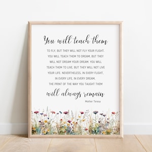 May include: A framed print featuring a quote by Mother Teresa, with the text "You will teach them." The quote is in black script on a white background, with a watercolor floral border at the bottom. The frame is light brown.
