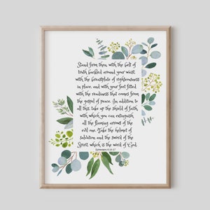 May include: A framed print featuring the scripture from Ephesians 6:14-17, surrounded by watercolor eucalyptus and greenery. The text is in a handwritten style, with a light beige frame.