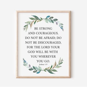 May include: A framed print with the text "BE STRONG AND COURAGEOUS. DO NOT BE AFRAID; DO NOT BE DISCOURAGED, FOR THE LORD YOUR GOD WILL BE WITH YOU WHEREVER YOU GO. Joshua 1:9." The text is surrounded by a watercolor wreath.