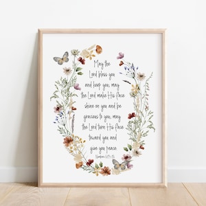 May include: A framed print featuring a floral wreath with butterflies and the text "May the Lord bless you and keep you..." from Numbers 6:24-26. The artwork has a light wooden frame and a white background, with watercolor-style flowers in various colors.