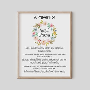 以下が含まれることがあります： 「A Prayer For Social Workers」のテキストが入った額入りのプリント。パステルカラーの花輪が「Social Workers」の文字を囲んでいます。祈りの言葉は黒色のエレガントなフォントで書かれています。