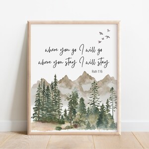 May include: A framed wall art print featuring a watercolour landscape of green pine trees and brown mountains. The text reads: where you go I will go where you stay I will stay Ruth 1:16. Four small grey birds are flying in the upper right corner.