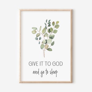 Può includere: Una stampa da parete incorniciata con un'illustrazione ad acquerello di foglie di eucalipto verdi centrata sopra il testo nero GIVE IT TO GOD and go to sleep. La stampa è racchiusa in una cornice di legno chiaro su sfondo bianco.