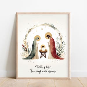 Puede incluir: Una ilustración de acuarela de la Sagrada Familia, María, José y el niño Jesús, en un pesebre. La imagen está rodeada por una corona de vegetación y estrellas doradas. El texto "a thrill of hope, the weary world rejoices" está debajo de la imagen.