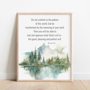 May include: A framed print with a light wood frame. The artwork features a watercolor landscape with mountains, trees, and a lake. The text reads: "Do not conform to the pattern of this world...Romans 12:2."
