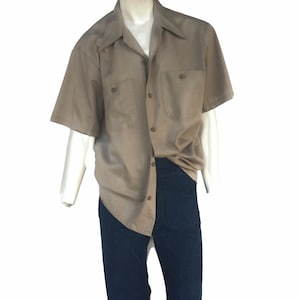 May include: A short-sleeved, light brown button-down shirt with two chest pockets and a button-up collar.