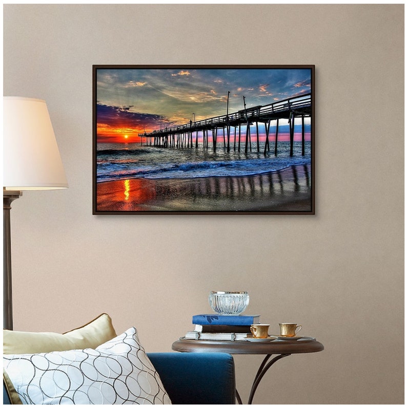May include: A photograph of a wooden pier extending into the ocean at sunset. The sky is a vibrant mix of pink, orange, and purple hues, with clouds reflecting in the water. The pier is silhouetted against the colorful sky, creating a dramatic scene.