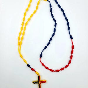 May include: A knotted rosary necklace with a cross pendant. The beads are yellow, blue and red, resembling a flag.