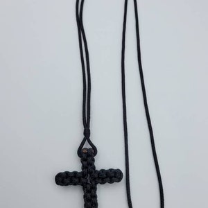 Puede incluir: Un collar de cuerda anudada negra con un colgante de cruz anudada negra.