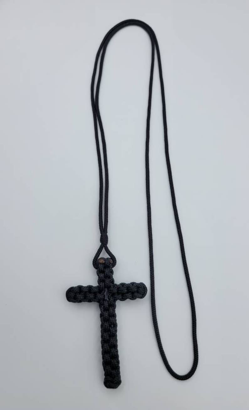 Puede incluir: Un collar de cuerda anudada negra con un colgante de cruz anudada negra.