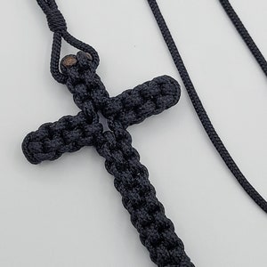 May include: A black knotted rope cross pendant on a black cord necklace.