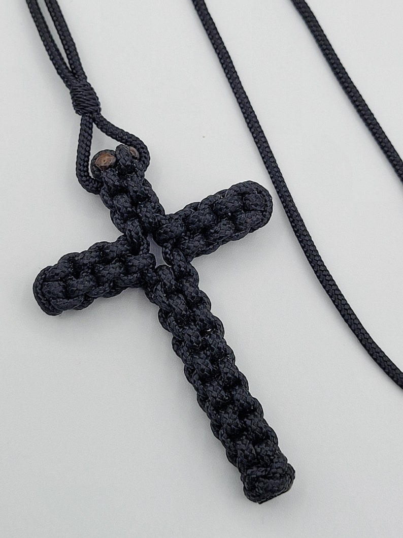 Puede incluir: Un colgante de cruz de cuerda anudada negra en un collar de cord&oacute;n negro.