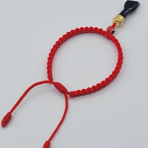 May include: Red string bracelet with a black hand charm and a blue evil eye bead.