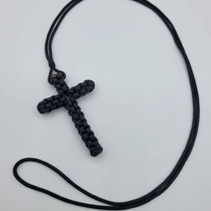 Puede incluir: Un collar de cord&oacute;n negro anudado con un colgante de cruz negra anudada.