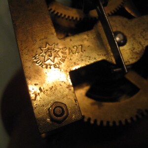 May include: Close-up of a brass clock mechanism with a star-shaped logo that reads "Wurttemberg A27".