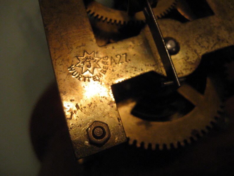 May include: Close-up of a brass clock mechanism with a star-shaped logo that reads "Wurttemberg A27".