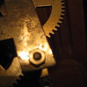 May include: Close-up of a brass gear mechanism with a visible number "7168" on the side. The gears are worn and have a golden patina.
