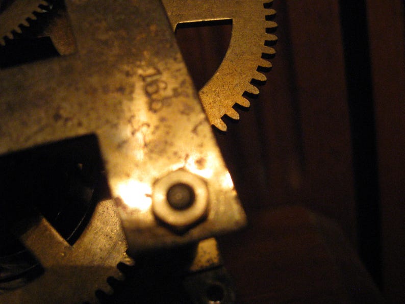 May include: Close-up of a brass gear mechanism with a visible number "7168" on the side. The gears are worn and have a golden patina.